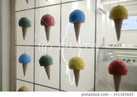 Decorative ice cream cones with colorful scoops hang inside a shop window. Decorative ice cream cones with colorful scoops hang inside a shop window. 141385685
