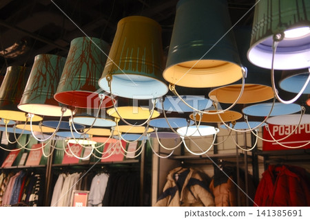 Rows of decorative metal buckets with paint drips hang as light fixtures in a clothing store Rows of decorative metal buckets with paint drips hang as light fixtures in a clothing store 141385691