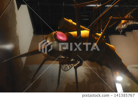 Mechanical insect art piece with illuminated red eyes and a long proboscis suspended indoors Mechanical insect art piece with illuminated red eyes and a long proboscis suspended indoors 141385767