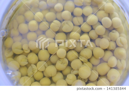 Many round green peas are submerged in clear liquid inside a transparent glass container 141385844