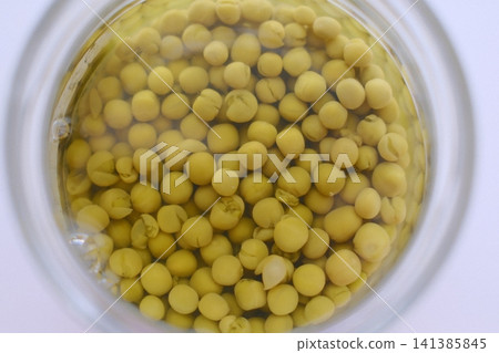 Round yellow green peas submerged in clear liquid within a glass jar Round yellow green peas submerged in clear liquid within a glass jar 141385845