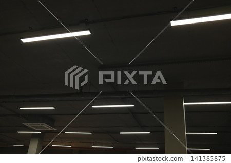 Multiple linear lights illuminate a dark concrete ceiling in an underground parking garage Multiple linear lights illuminate a dark concrete ceiling in an underground parking garage 141385875