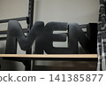 Black MEN sign on wood shelf in clothing store, plaid shirt to right 141385877