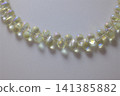 A string of clear, iridescent teardrop glass beads shines with soft colors against a bright white surface 141385882