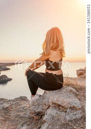 Woman sunset cliff sitting on a rocky ledge overlooking the sea during a peaceful golden hour moment in nature 141386051