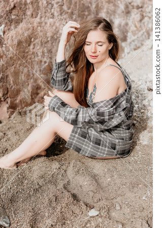 Woman beach relaxation sitting on a sandy shoreline in an oversized shirt reflecting during a peaceful summer vacation Woman beach relaxation sitting on a sandy shoreline in an oversized shirt reflecting during a peaceful summer vacation 141386062