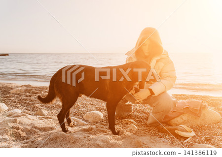 Dog woman beach caring for companion black dog during warm golden hour on rocky seashore. Dog woman beach caring for companion black dog during warm golden hour on rocky seashore. 141386119