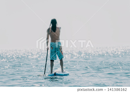 Paddleboarding Man Ocean Water Sport - A man paddleboards on a calm ocean in a blue swimsuit. 141386162