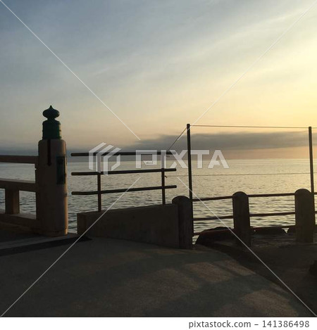 The sunset silhouettes of the railings and ornamental finials of a bridge by the sea. The sunset silhouettes of the railings and ornamental finials of a bridge by the sea. 141386498