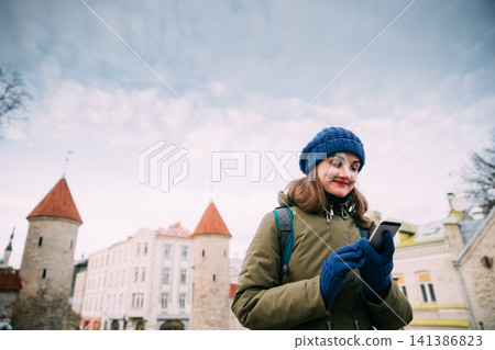 Tallinn, Estonia. Young Caucasian Confident Woman Backpacker Tourist Using Smartphone Near Landmark Viru Gate. Vacation In Old Town. Girl Surfing Net Internet In Phone 141386823