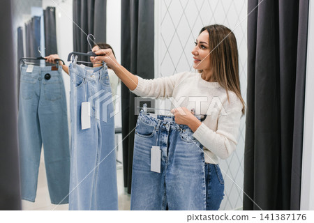 Happy Woman Choosing Trendy Jeans in Fitting Room Happy Woman Choosing Trendy Jeans in Fitting Room 141387176