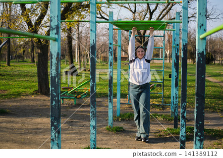Teen girl exercising on outdoor gym in park Teen girl exercising on outdoor gym in park 141389112
