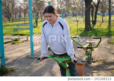 Teen girl exercising on outdoor gym in park Teen girl exercising on outdoor gym in park 141389113