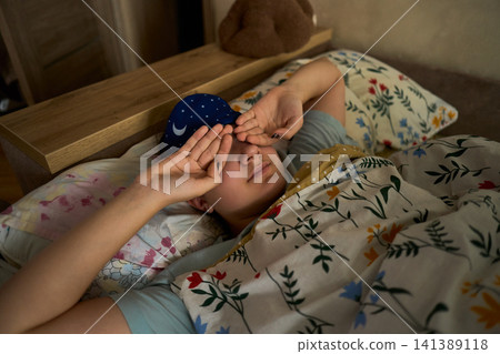 Teen waking up in bed with sleep mask 141389118