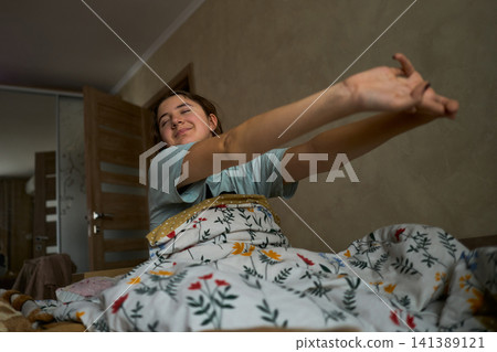 Teen girl stretching in bed after waking Teen girl stretching in bed after waking 141389121