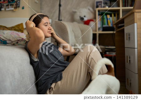 Teen girl relaxing with headphones and dog Teen girl relaxing with headphones and dog 141389129