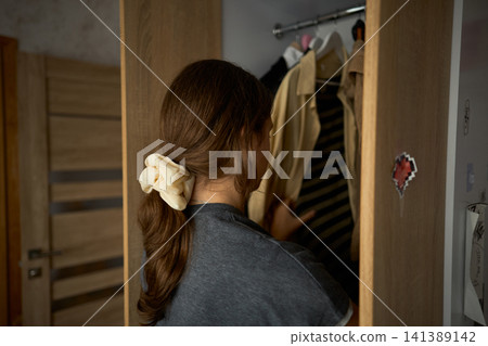 Teen girl searching clothes in open wardrobe Teen girl searching clothes in open wardrobe 141389142