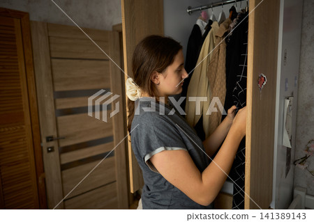 Teen girl searching clothes in open wardrobe 141389143