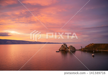 Wide landscape of Lake Baikal at sunset with pink and purple clouds. Shamanka Rock on Olkhon Island surrounded by boats. Colorful evening sky and water for background Wide landscape of Lake Baikal at sunset with pink and purple clouds. Shamanka Rock on Olkhon Island surrounded by boats. Colorful evening sky and water for background 141389716