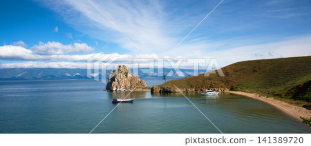 Panoramic view of Shamanka rock on Lake Baikal. Sandy beach and grassy hills on Olkhon island with boats anchored in the water. Summer landscape of Siberian nature in Russia Panoramic view of Shamanka rock on Lake Baikal. Sandy beach and grassy hills on Olkhon island with boats anchored in the water. Summer landscape of Siberian nature in Russia 141389720