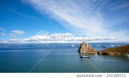 Wide landscape view of Olkhon island in Lake Baikal. Small blue boat on deep water with mountains in the background. Summer travel destination in Siberia, Russia Wide landscape view of Olkhon island in Lake Baikal. Small blue boat on deep water with mountains in the background. Summer travel destination in Siberia, Russia 141389721
