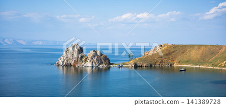 Panoramic view of Shamanka Rock on Olkhon Island. Twin-peaked rock formation and grassy peninsula in Lake Baikal. Wide landscape, nature of Russia Panoramic view of Shamanka Rock on Olkhon Island. Twin-peaked rock formation and grassy peninsula in Lake Baikal. Wide landscape, nature of Russia 141389728