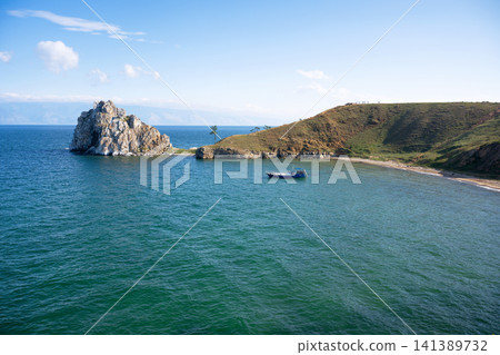 Summer landscape of Lake Baikal with Shamanka Rock and a blue boat in the bay. Grassy peninsula and clear sky during daytime, Olkhon Island in Russia 141389732