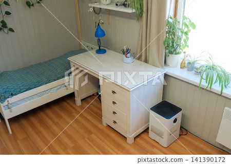 Bright school boy room with desk sunlit white desk beside bed, blue lamp, potted plants on windowsill, patterned bedspread, wooden floor, neat storage, calm study atmosphere. Learning environment Bright school boy room with desk sunlit white desk beside bed, blue lamp, potted plants on windowsill, patterned bedspread, wooden floor, neat storage, calm study atmosphere. Learning environment 141390172