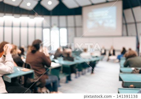 A large group of diverse people attending a professional presentation or educational workshop in a modern lecture hall. Defocus image of audience from behind. A large group of diverse people attending a professional presentation or educational workshop in a modern lecture hall. Defocus image of audience from behind. 141391138