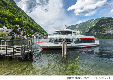 Passenger boat cruising on Lake Hallstatt with mountain landscape in Austria, illustrating scenic summer tourism in Europe. Passenger boat cruising on Lake Hallstatt with mountain landscape in Austria, illustrating scenic summer tourism in Europe. 141391771