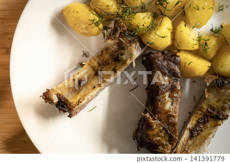 Barbecue ribs with potatoes and dill served on a wooden table, creating a home atmosphere with casual comfort food. 141391779