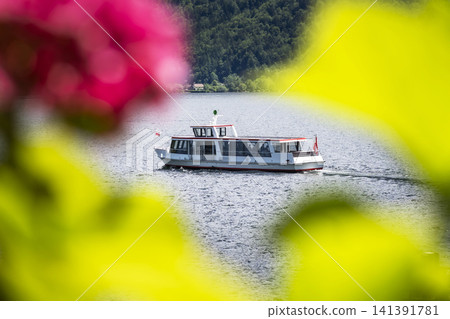 Boat cruising on Lake Hallstatt in Austria with blurred floral foreground, illustrating scenic summer lake tourism in Europe. Boat cruising on Lake Hallstatt in Austria with blurred floral foreground, illustrating scenic summer lake tourism in Europe. 141391781