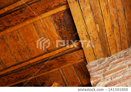 Rustic wooden ceiling with exposed beam and brick wall interior detail. Weathered wooden ceiling panels in an old rustic Esotonian house 141391808