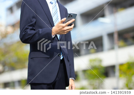 一位二十多歲的商人手持智慧型手機在戶外。 一位二十多歲的商人手持智慧型手機在戶外。 141391939