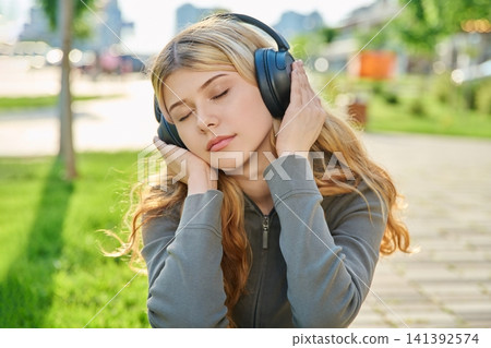 Young woman listening to music in black wireless headphones with eyes closed Young woman listening to music in black wireless headphones with eyes closed 141392574