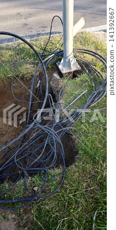 Cable wires tangled near a utility pole in a grassy area by a road 141392667
