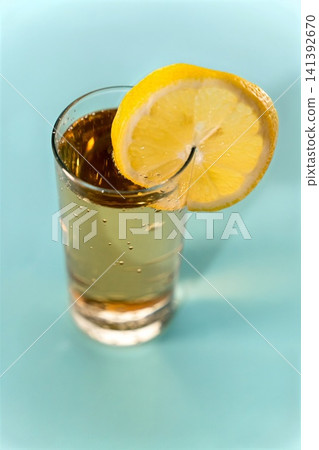 Fresh lemonade served in a clear glass with a lemon slice on a blue surface Fresh lemonade served in a clear glass with a lemon slice on a blue surface 141392670