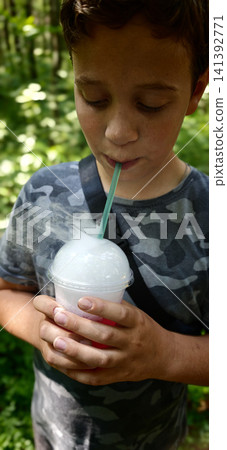 Child enjoys a cold drink while standing in a green outdoor area Child enjoys a cold drink while standing in a green outdoor area 141392771