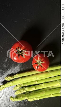 Food ingredients: asparagus and cherry tomatoes arranged against a black background. Food ingredients: asparagus and cherry tomatoes arranged against a black background. 141393411