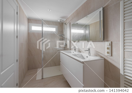 Modern bathroom interior with double vanity, large wall mirror, frameless glass shower, chrome fixtures, beige tile, bright natural light, clean minimalist residential design Modern bathroom interior with double vanity, large wall mirror, frameless glass shower, chrome fixtures, beige tile, bright natural light, clean minimalist residential design 141394042