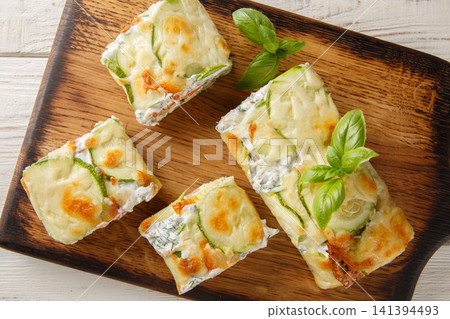 Close-up of sliced zucchini roll stuffed with salmon and cream cheese on a wooden board. Horizontal top view Close-up of sliced zucchini roll stuffed with salmon and cream cheese on a wooden board. Horizontal top view 141394493