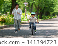 A young boy practicing riding a bicycle with his mother. 141394723
