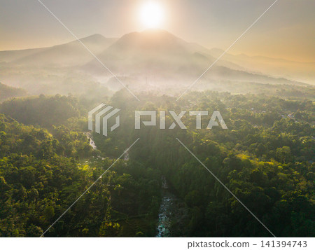 Aerial view of the lush Tegalalang landscape featuring a winding river flowing through dense tropical forest and terraced fields in Indonesia Aerial view of the lush Tegalalang landscape featuring a winding river flowing through dense tropical forest and terraced fields in Indonesia 141394743