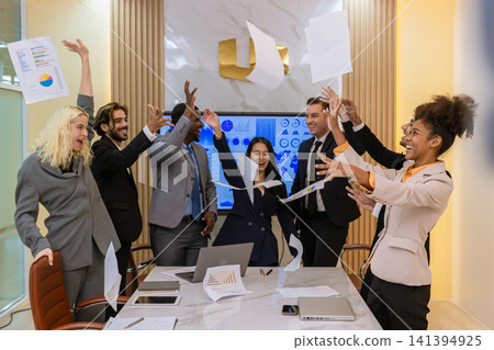 A multi-ethnic professional team celebrating a project completion by tossing papers in the air at a modern boardroom, expressing joy, teamwork, and corporate achievement. A multi-ethnic professional team celebrating a project completion by tossing papers in the air at a modern boardroom, expressing joy, teamwork, and corporate achievement. 141394925