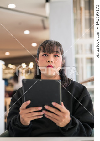 Thai Transgender Woman Holding Digital Tablet and Looking Ahead Indoors 141395173