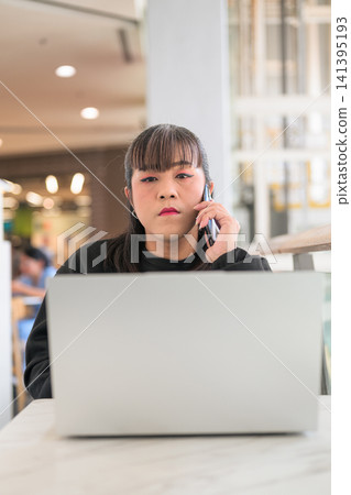Thai Transgender Woman Talking on Smartphone Behind Laptop Indoors Thai Transgender Woman Talking on Smartphone Behind Laptop Indoors 141395193
