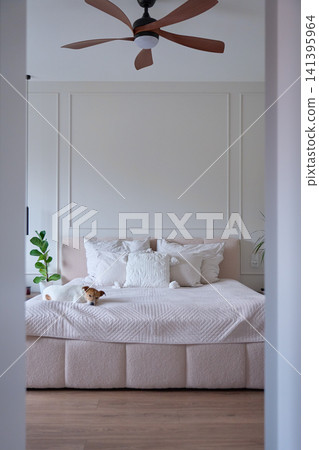 Bright bedroom featuring ceiling fan above neatly made bed with plants and simple furnishings 141395964