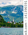 St. Martin Parish Church in Bled, Slovenia, with the majestic Julian Alps rising in the background, showcasing Neo-Gothic architecture in a spectacular alpine setting. 141396591