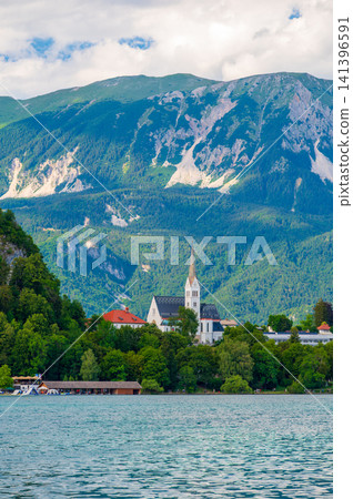St. Martin Parish Church in Bled, Slovenia, with the majestic Julian Alps rising in the background, showcasing Neo-Gothic architecture in a spectacular alpine setting. St. Martin Parish Church in Bled, Slovenia, with the majestic Julian Alps rising in the background, showcasing Neo-Gothic architecture in a spectacular alpine setting. 141396591