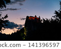 Low-angle view of Bled Castle perched on a rocky cliff above Lake Bled, Slovenia, beneath a dramatic dark sky after sunset, highlighting its medieval architecture. 141396597